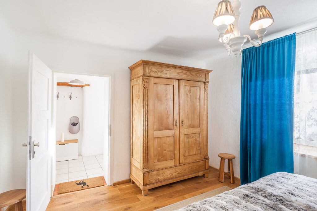 alter hochwertiger Kleiderschrank aus Holz, Hocker und blauen Vorhängen im Schlafzimmer