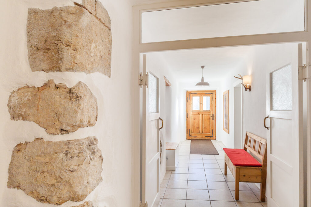 Der Eingangsbereich mit Sitzbank, Naturstein in die Wand eingearbeitet und Blick auf die Holz-Haustür